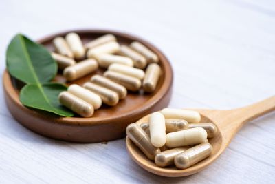 capsules in a spoon next to a capsules bowl with a leaf