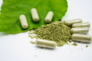 kratom powder surrounded by filled capsules and a kratom leaf