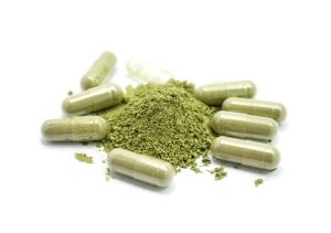 Pile of kratom powder and capsules on white background