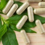 kratom capsules laying on fresh leaf on wooden table