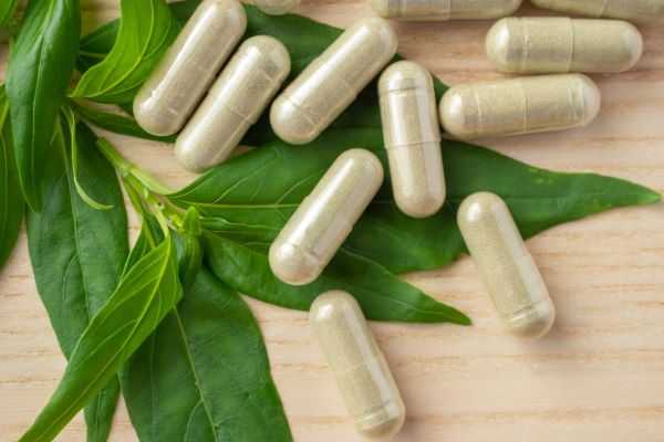 kratom capsules laying on fresh leaf on wooden table