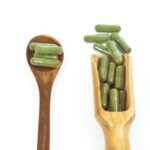 Kratom capsules on different size spoons. One is a small spoon with 4 capsules. The other is a larger dosing spoon holding 12 capsules