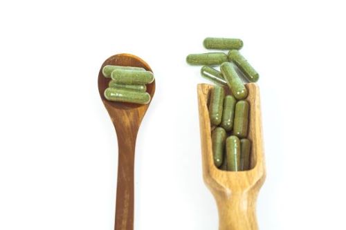 Kratom capsules on different size spoons. One is a small spoon with 4 capsules. The other is a larger dosing spoon holding 12 capsules