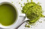 kratom powder on a spoon next to a cup of kratom tea on a table.