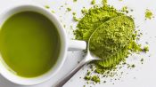 kratom powder on a spoon next to a cup of kratom tea on a table.