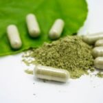 kratom powder surrounded by filled capsules and a kratom leaf