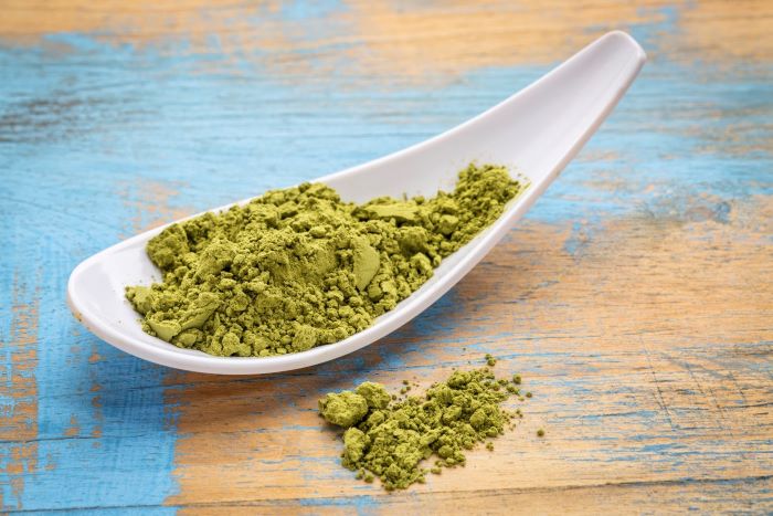 kratom powder on white spoon on colorful wooden table