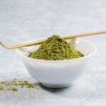 White bowl of kratom powder with a wooden stirrer sitting over bowl.