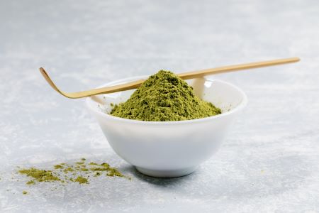 White bowl of kratom powder with a wooden stirrer sitting over bowl.