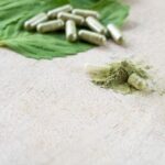 kratom powder bursting from a broken capsule laying on a dried kratom leaf