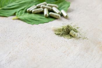 kratom powder bursting from a broken capsule laying on a dried kratom leaf